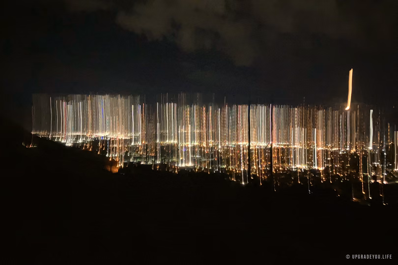 Warm city lights glowing in long streaks across a dark valley at night