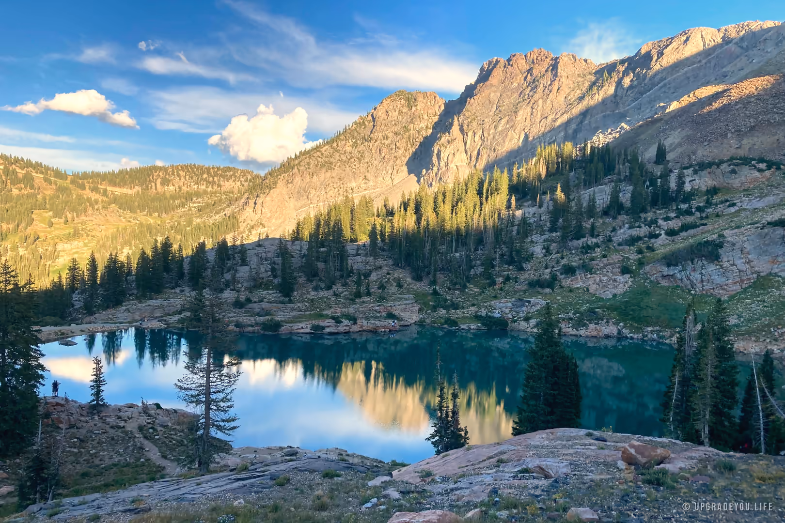 Cecret Lake, a teal alpine lake in the Utah mountains ringed by pines and rugged granite peaks under a clear sky