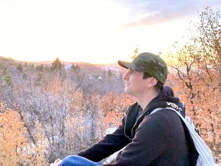 Jess sitting on a hillside at sunset, looking out over autumn oak and distant snow.
