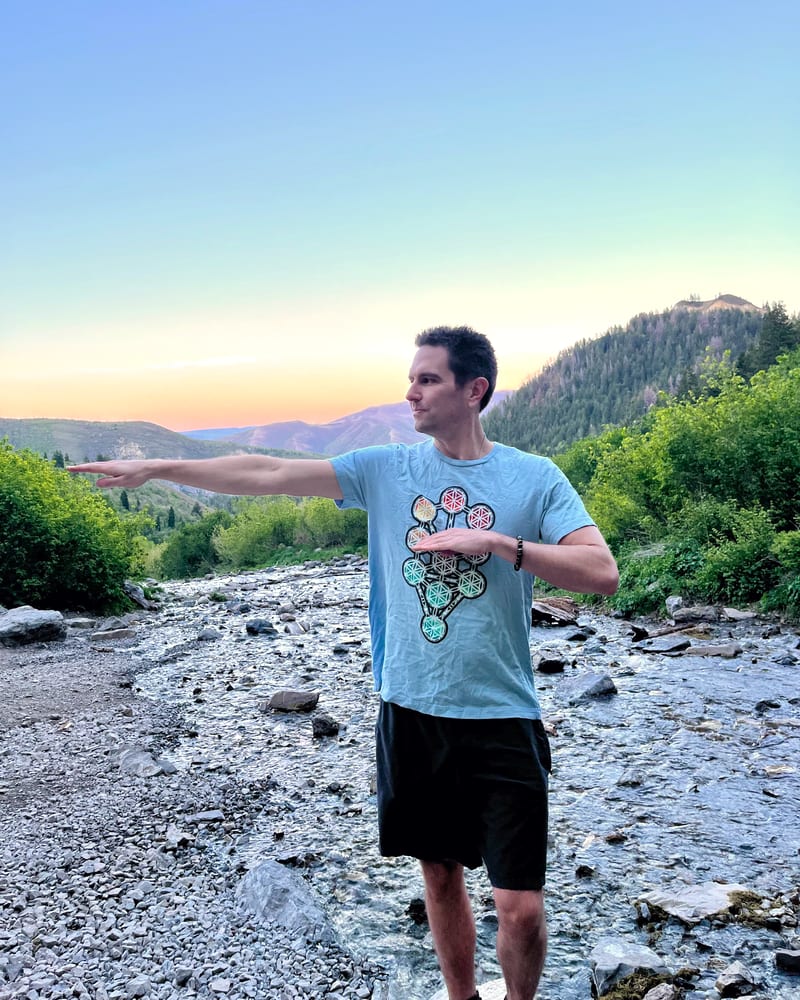 Jess standing in a mountain riverbed at sunset, one arm extended in a Qigong posture.
