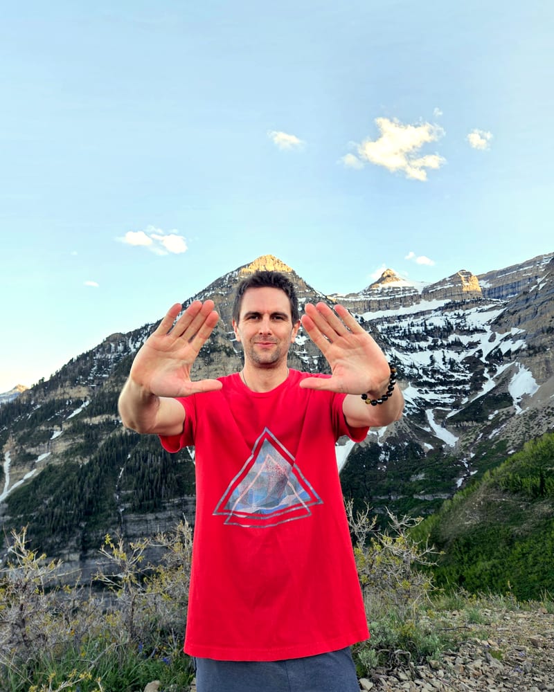 Jess holding both palms forward in a Qigong posture, snow-covered Mount Timpanogos behind him.