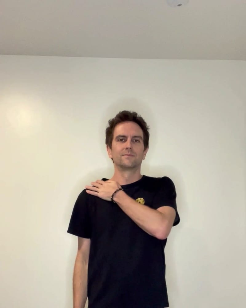 Jess demonstrating a lymphatic drainage movement, one hand resting on the opposite shoulder.