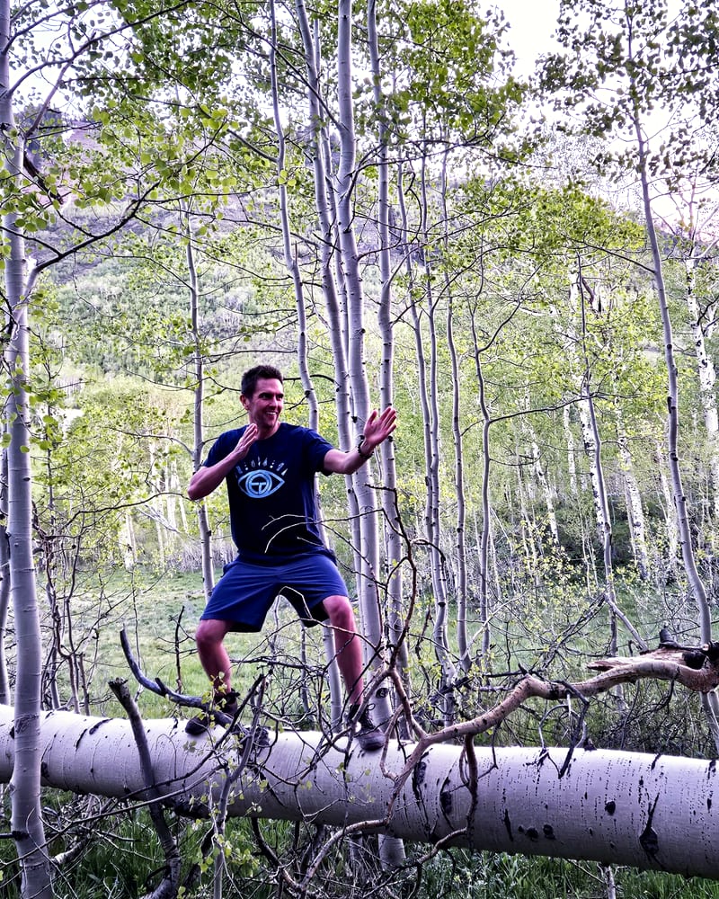 Jess balancing barefoot on a fallen aspen trunk in a grove of white aspens.